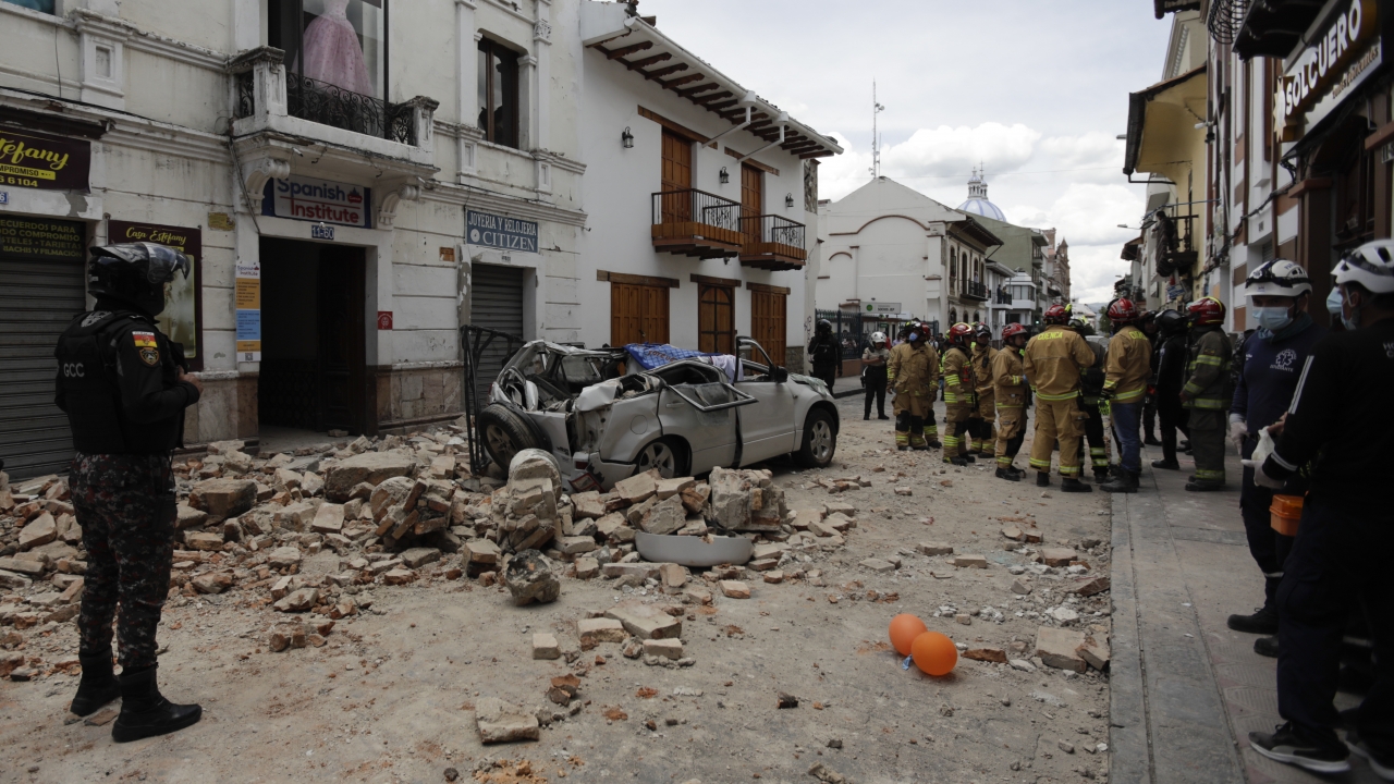 Rescue workers stand next to a car crushed by debris after an earthquake in Cuenca, Ecuador.