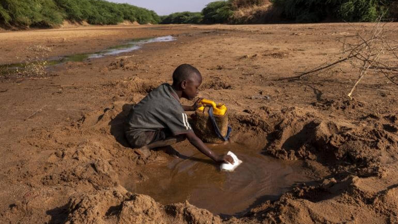 A boy in Africa dips a cloth in a muddy puddle.
