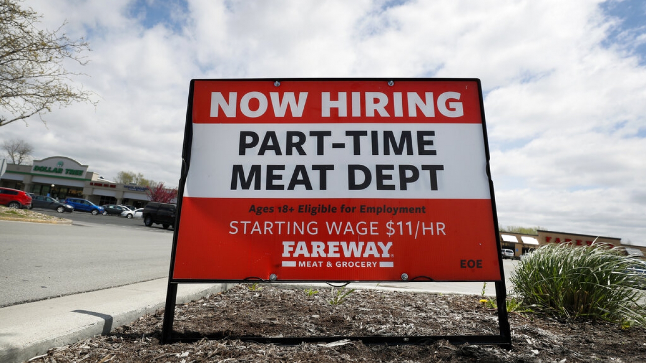 A now hiring sign is displayed in front of a grocery store.