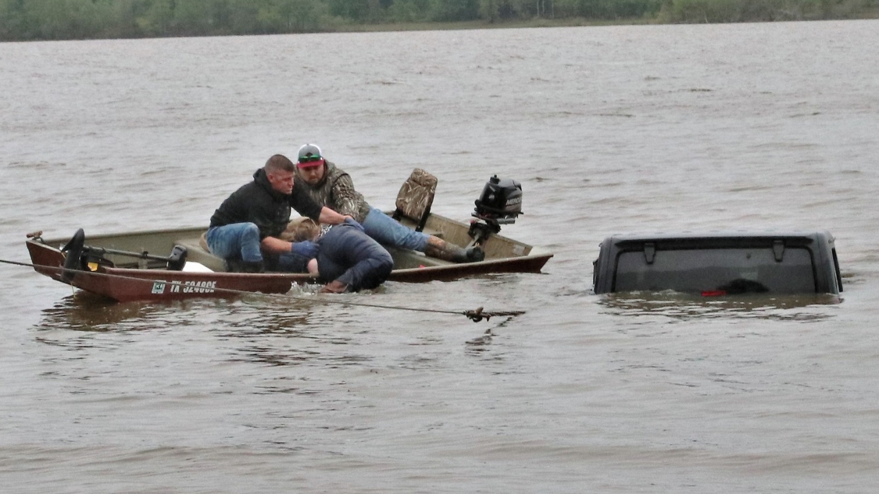 Two men on a boat help a woman escape her submerged Jeep.