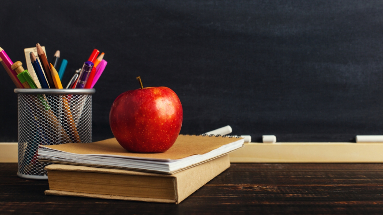 Image of a teacher's desk with books, pencils and an apple