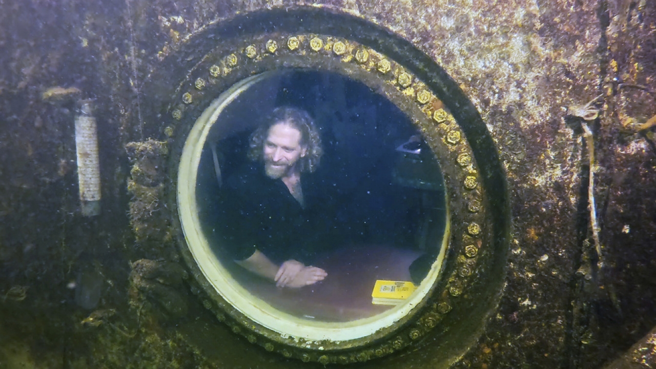 Dr. Joseph Dituri peers out of a large porthole in an undersea vessel.