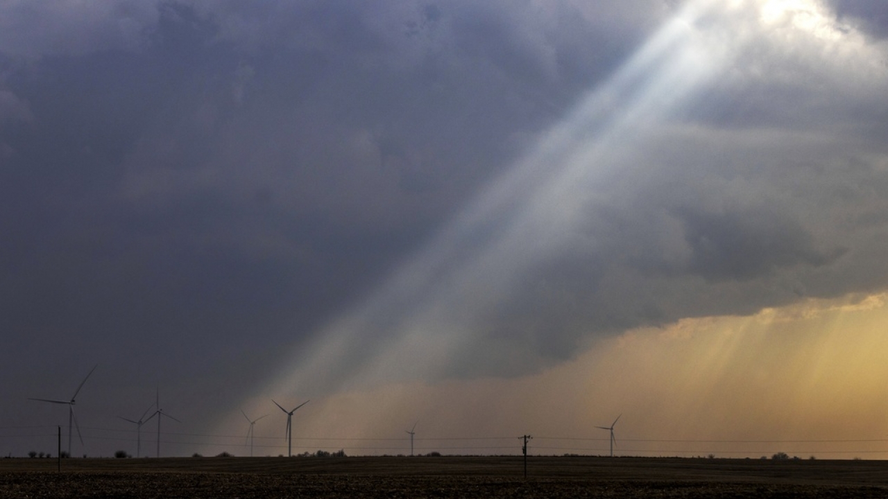 Sunlight filters through storm clouds onto a wind turbine