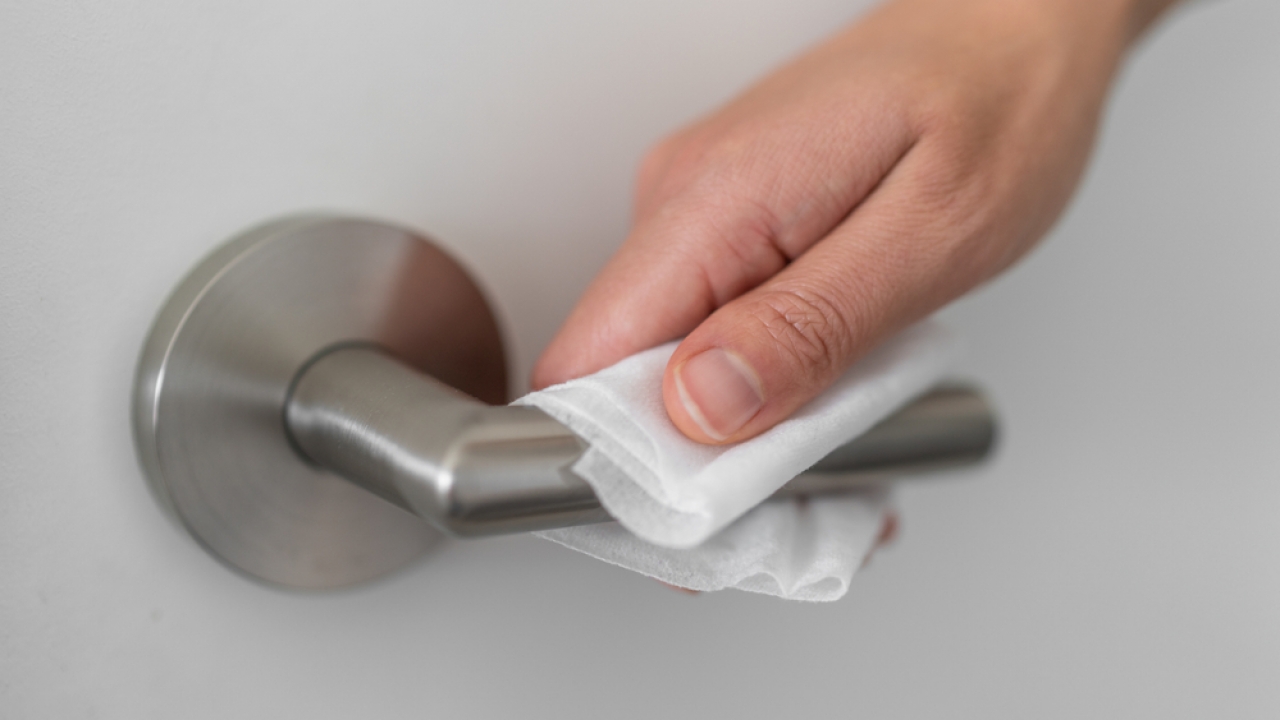 Person uses cleaning wipe on door handle.