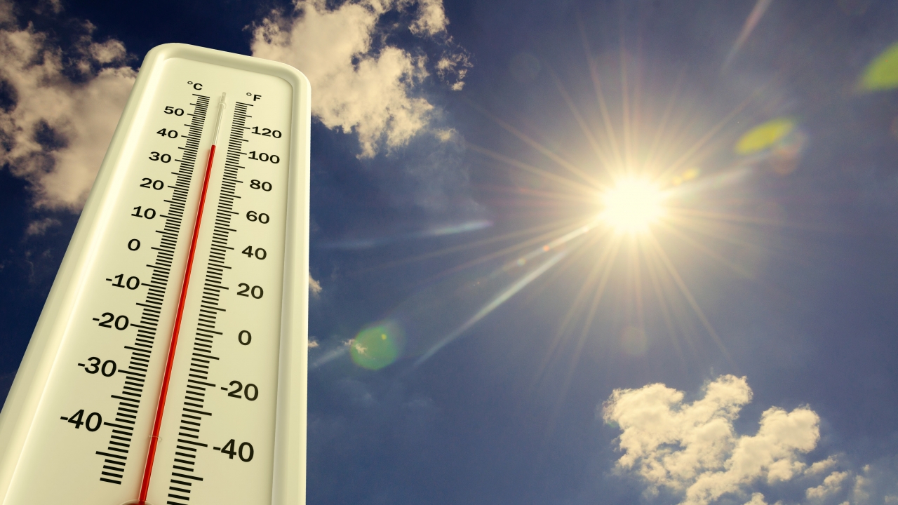 A thermometer at a high temperature is displayed in front of a sky with a beaming sun.
