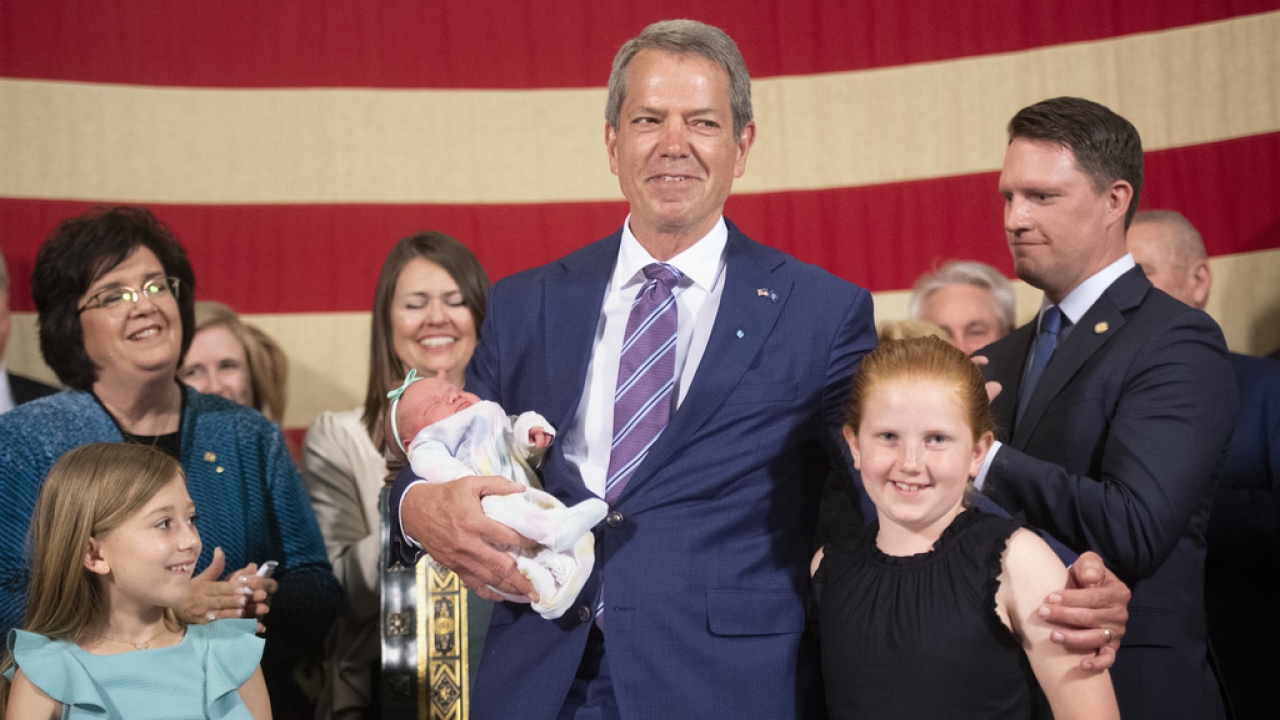 Nebraska Gov. Jim Pillen smiles as he holds a newborn next to his granddaughters.