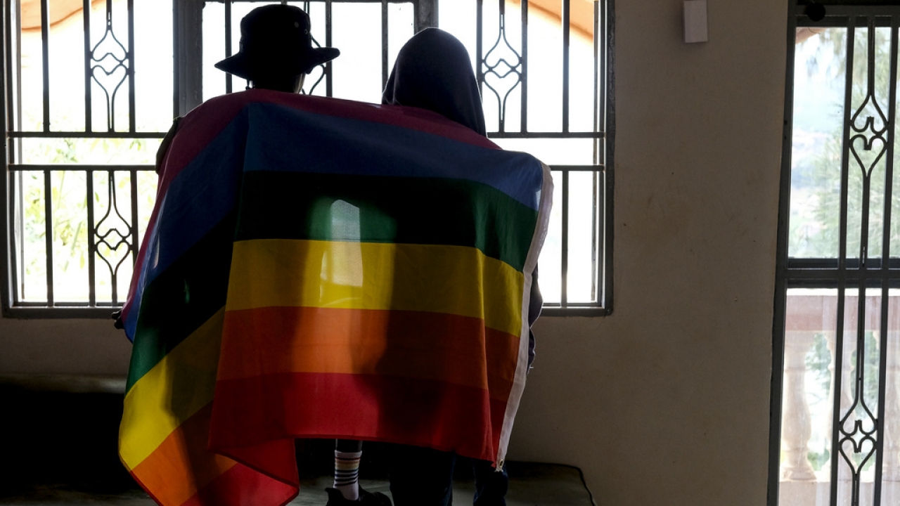 A gay Ugandan couple cover themselves with a pride flag as they pose for a photograph
