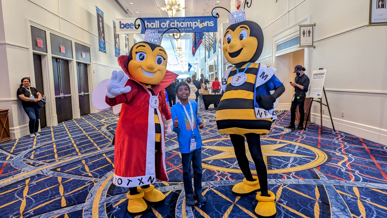 Vihaan Kapil poses with two Spelling Bee mascots.