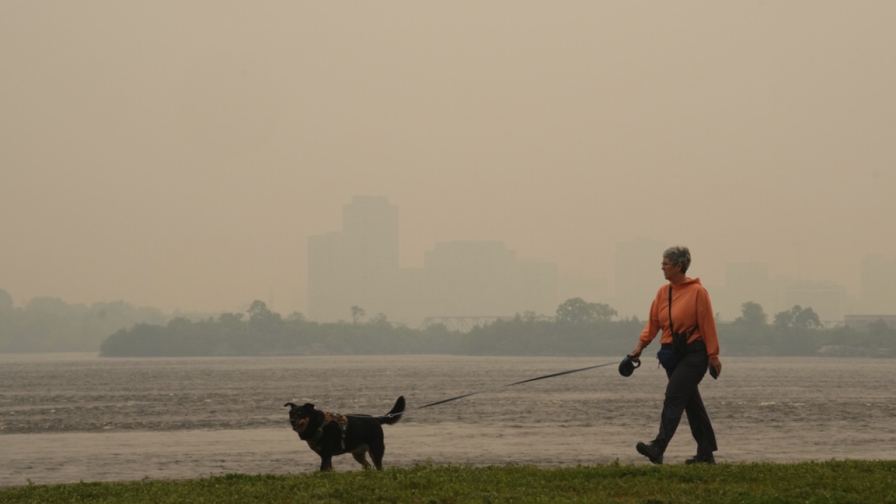 A woman walks her dog along the Ottawa River in Ottawa as smoke from wildfires obscures Gatineau, Que.