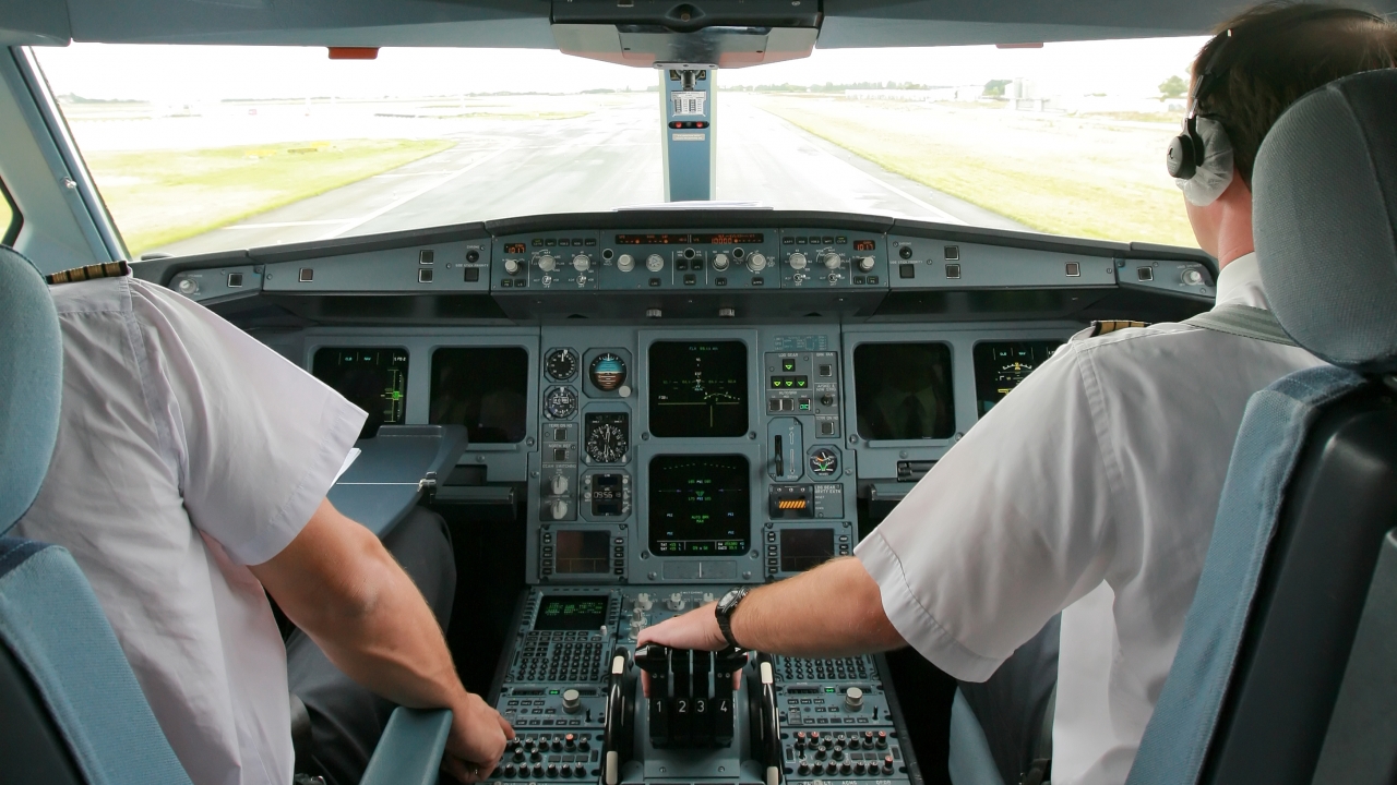 Two pilots in the cockpit of a plane on a runway.