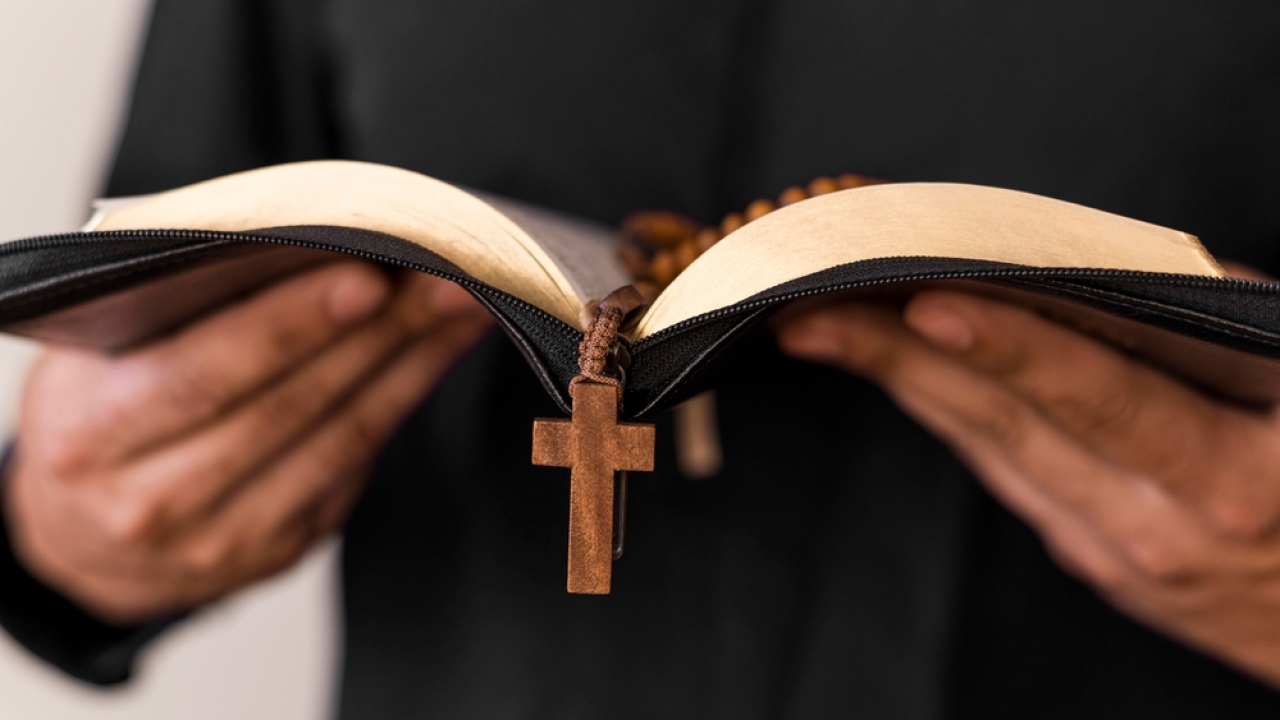 A person holds what appears to be a Bible with a cross hanging from it.