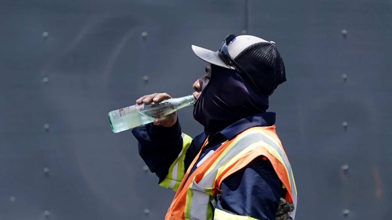 Standing in the mid afternoon heat, a worker takes a break to drink during a parking lot asphalt resurfacing job.