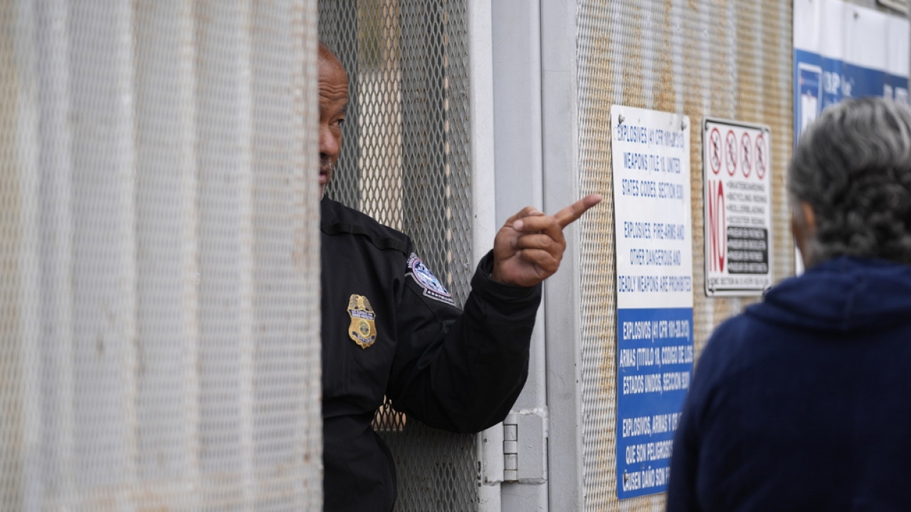 A United States Customs and Border Protection officer points toward a line of people waiting to apply for asylum.