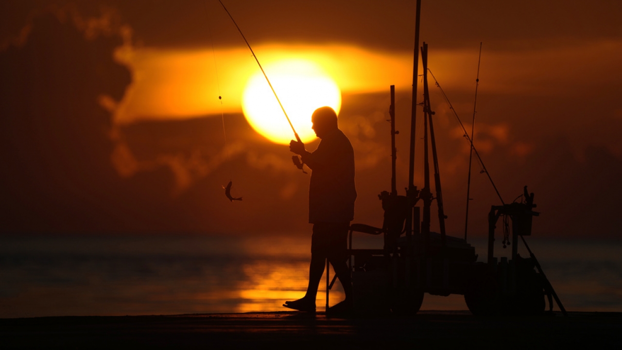 A fisherman reels in his catch as the sun rises.