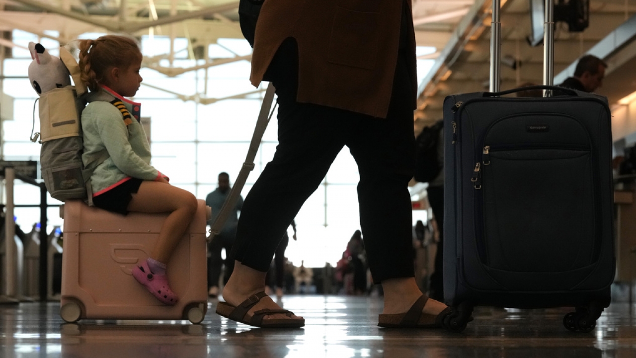 A young girl rides on wheeled luggage as she and a family member check in for their flight.
