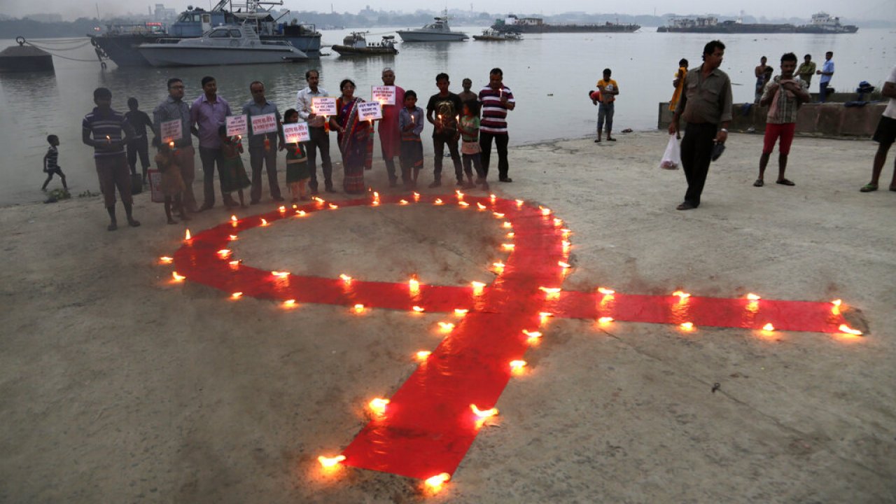 Volunteers stand with placards beside a huge red ribbon lighted with lamps during an AIDS awareness rally in India.