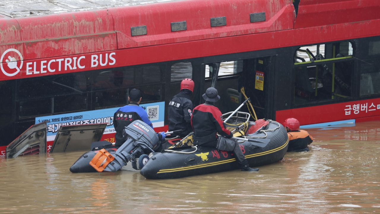A bus submerged in floodwaters as rescuers wade through on an inflatable boat