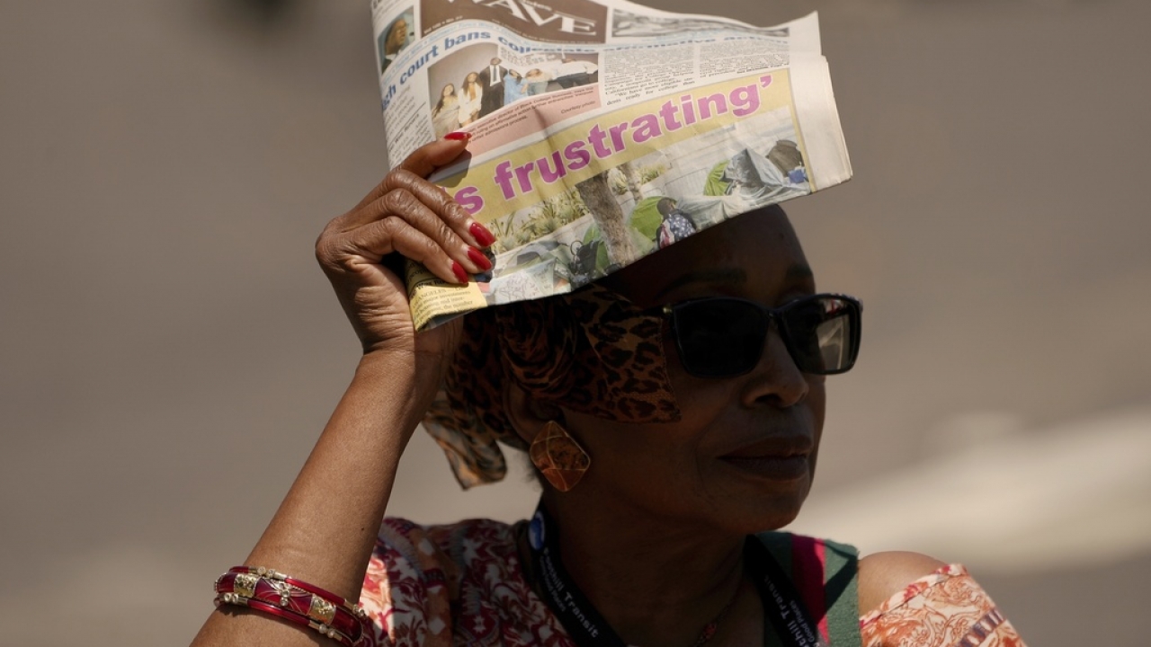 Woman uses a newspaper to shield herself from the sun.