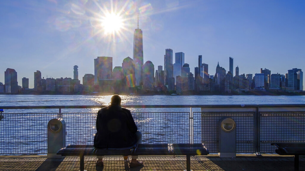 A person sits on a bench looking at the lower Manhattan skyline.