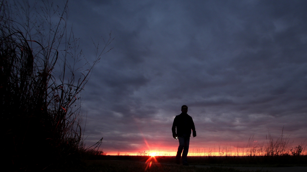 A man walks along a trail during sunset.