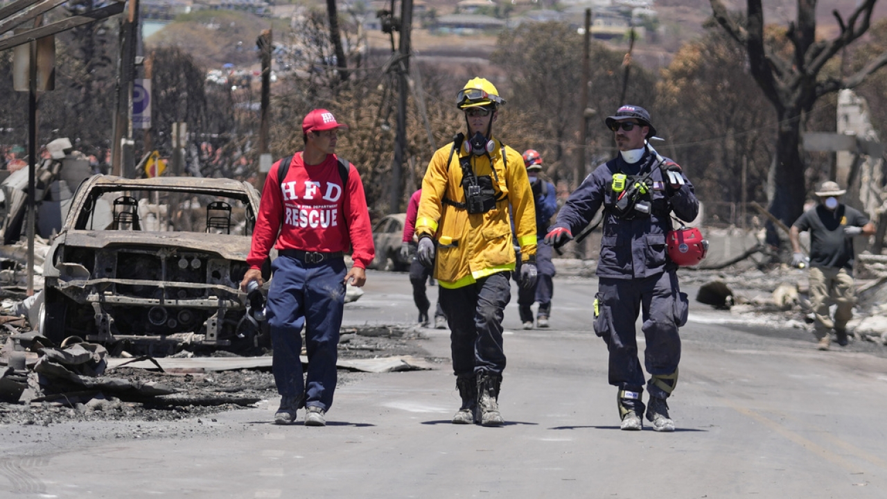Members of a search-and-rescue team walk next to rubble and a burnt car