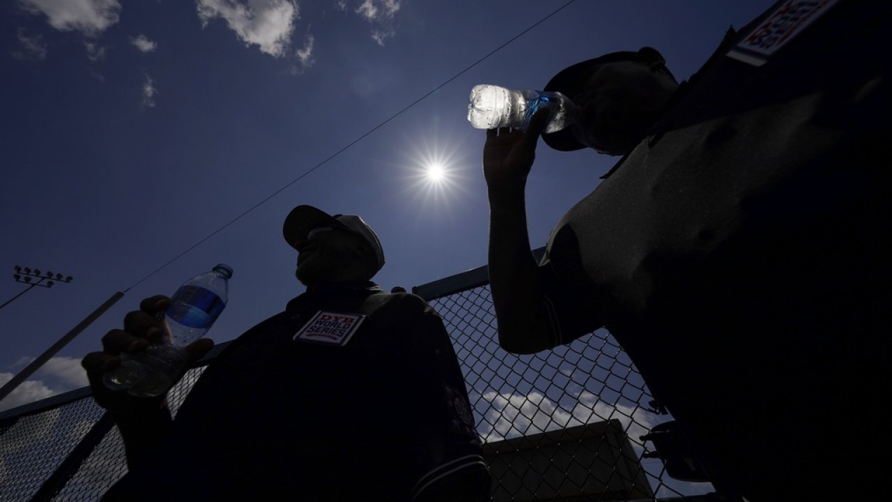 Youth baseball players drinking water under the hot sun.