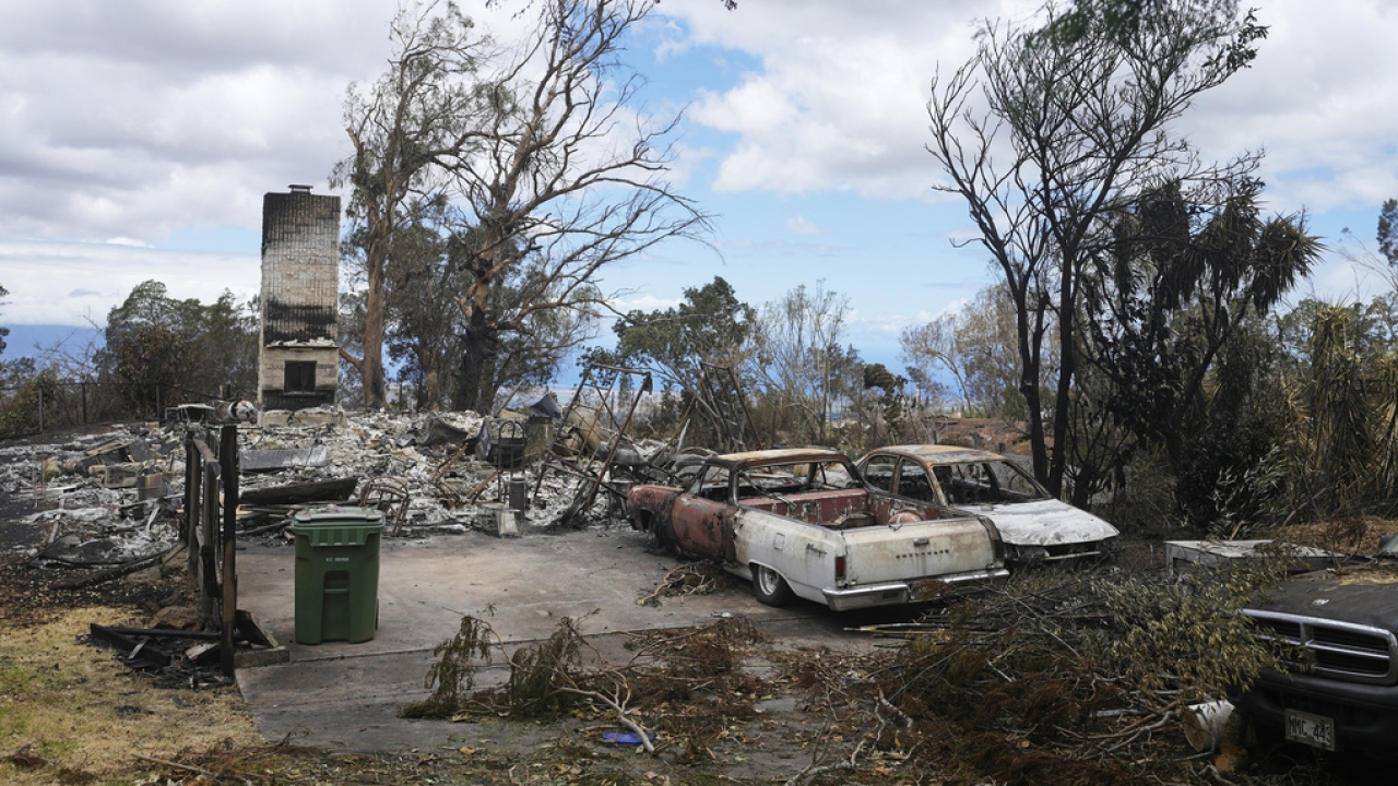 Charred vehicles sit near a wildfire-destroyed home