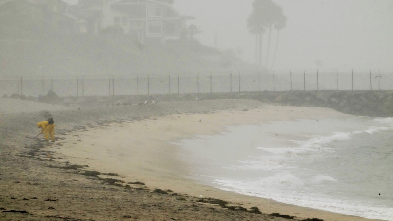 A person in rain gear looks through the sand at the beach during a storm.