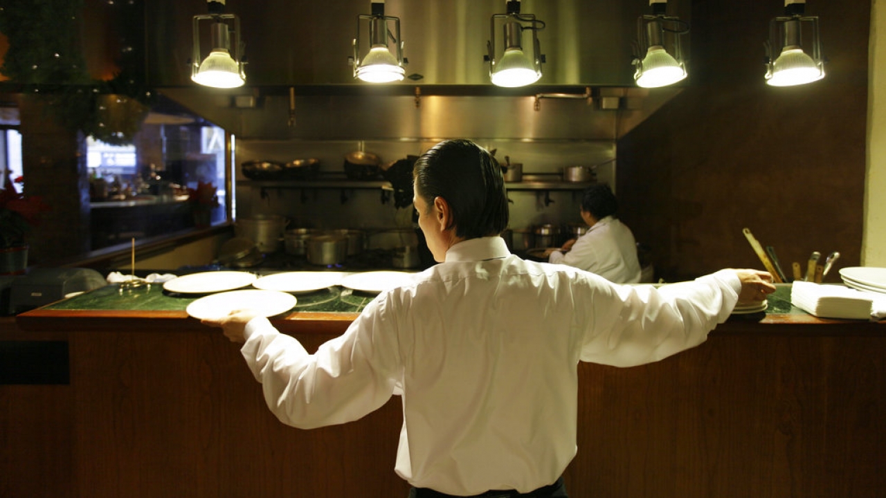 A waiter reaches for plates at a restaurant in San Francisco