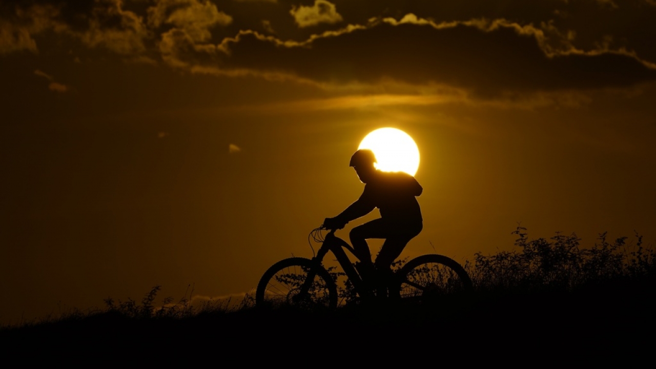 A cyclist tops a hill on a hot day at sunset.