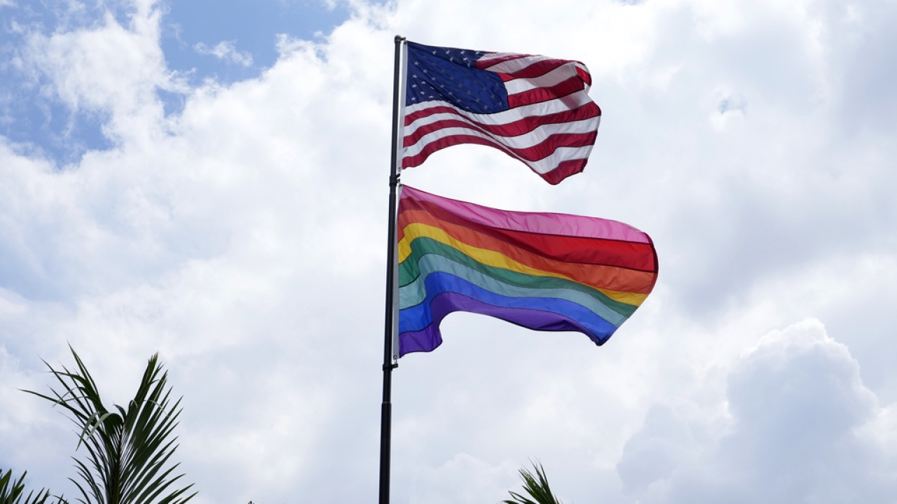 An American flag flies with a pride flag outside of a home.