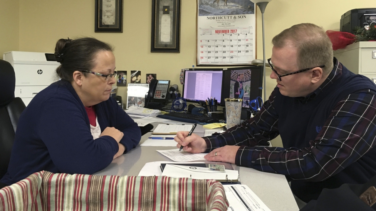 Former Kentucky county clerk Kim Davis looks on as David Ermold signs paperwork.