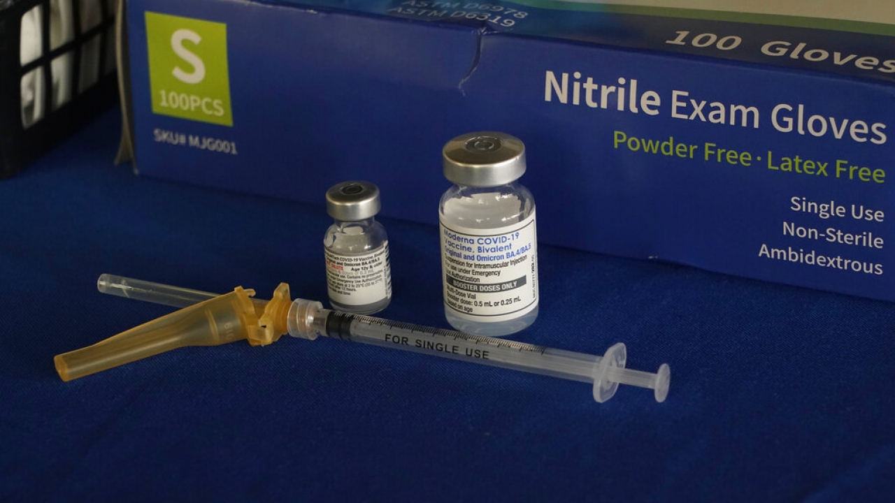A syringe lies next to Pfizer, left, and Moderna COVID-19 booster vaccines at an inoculation station.