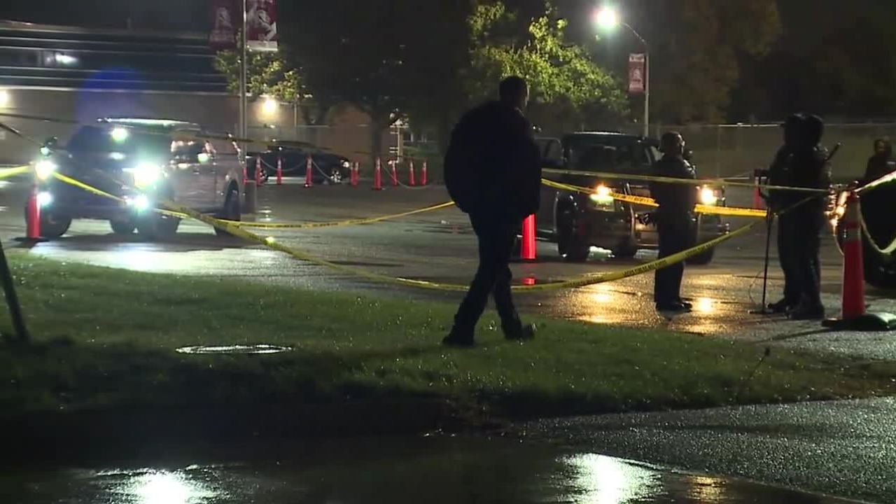 Police in a parking lot surrounded by caution tape investigate the scene of a shooting