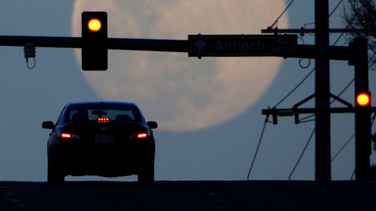 A motorist waits at a traffic light while the waxing full moon rises in the distance.