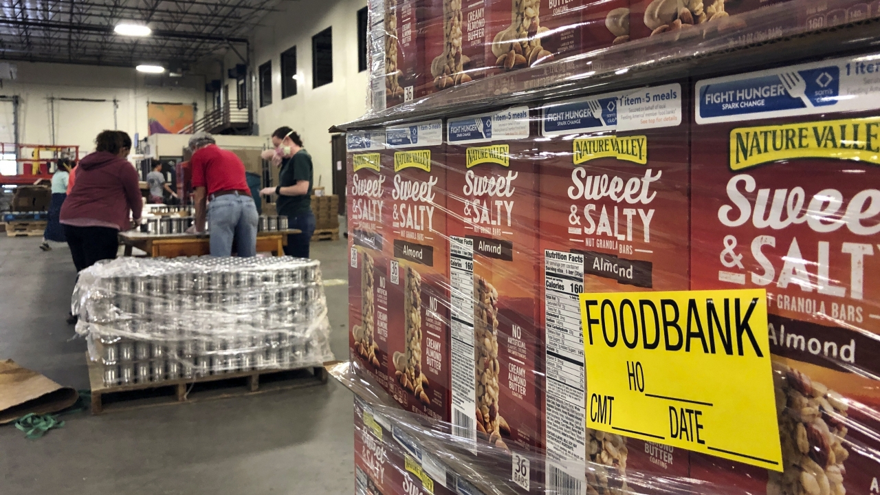A pallet of food awaits processing as volunteers work in the background to label cans of beans for redistribution May 7, 2020