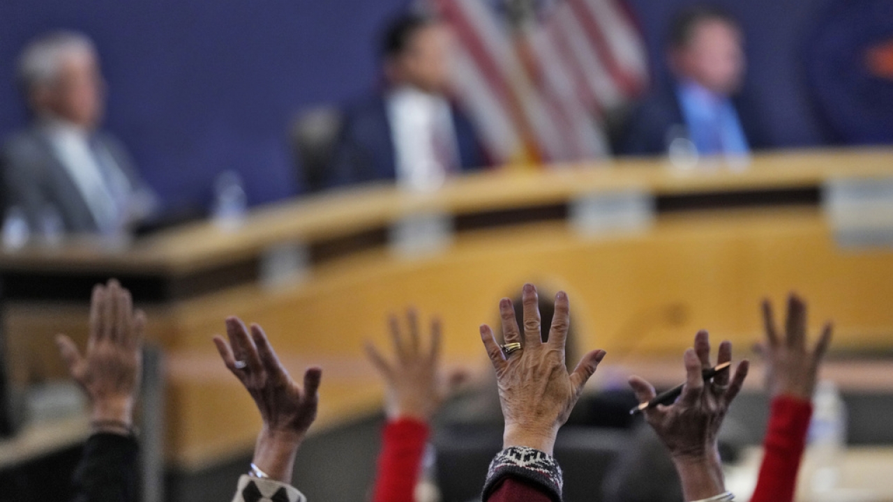 People wave their hands in protest during the Maricopa County Board of Supervisors meeting.