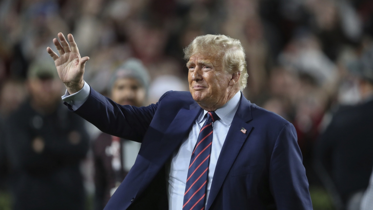 Former President Donald Trump waves during halftime of an NCAA college football game.
