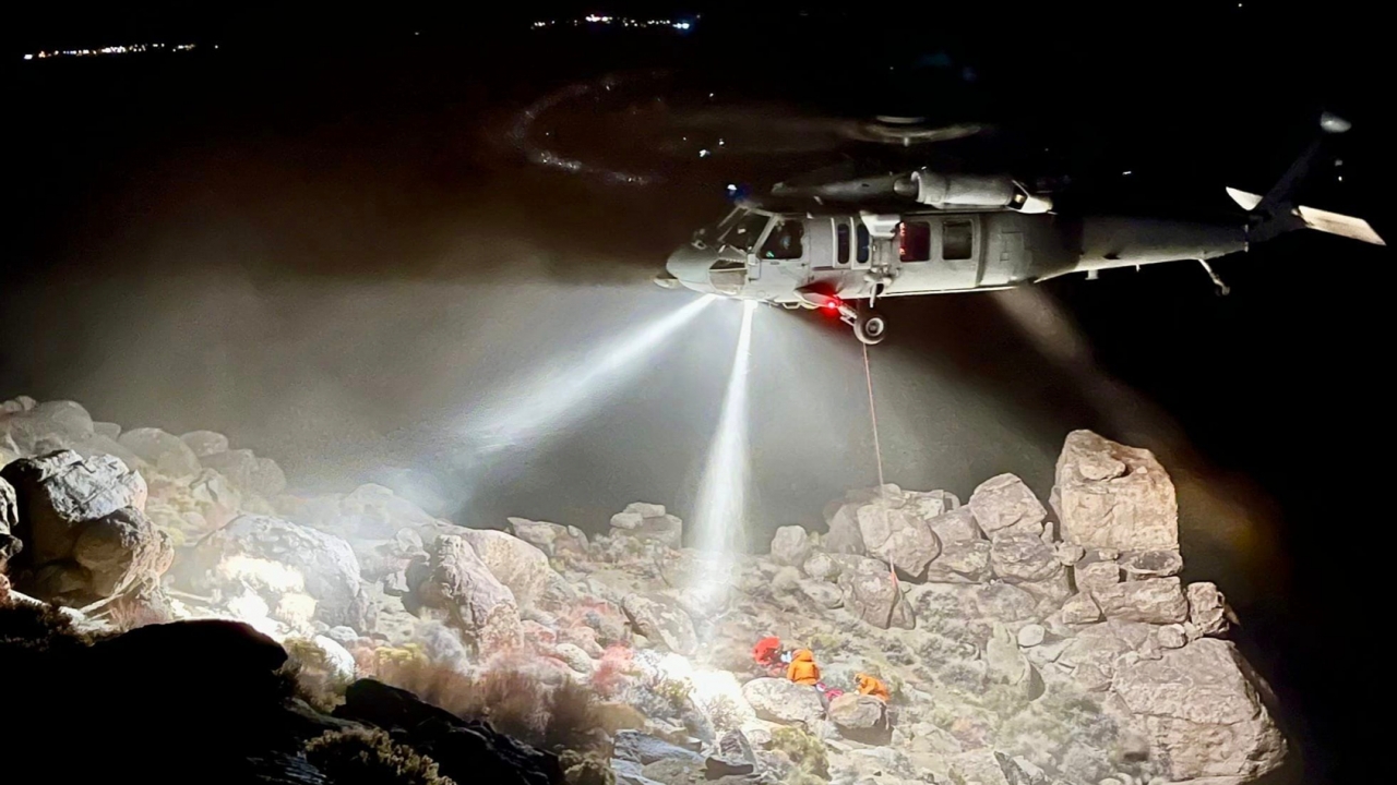 A helicopter hovers over a hiker trapped under a boulder.