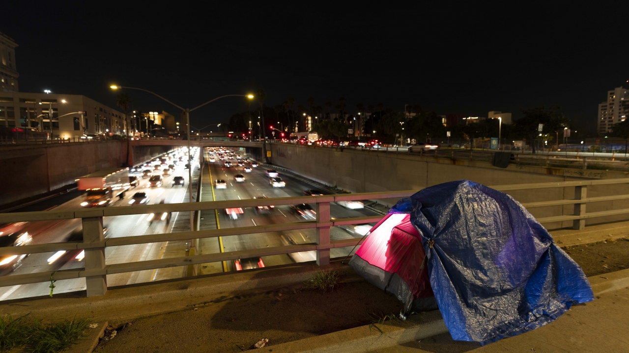 Tarp covers a portion of a homeless person's tent on a bridge.