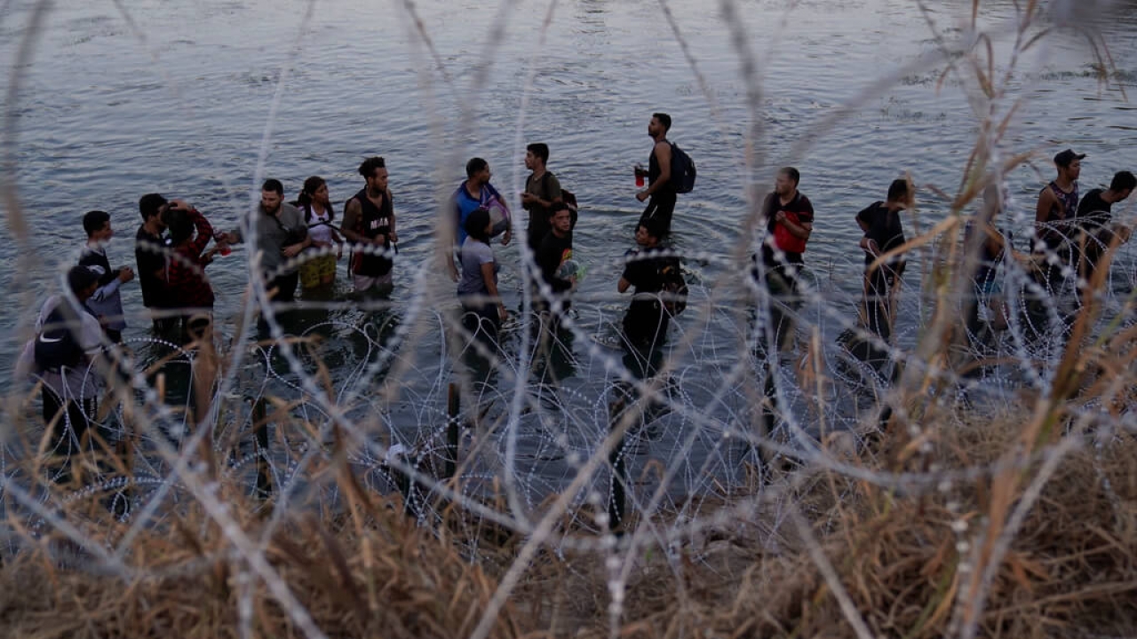 Migrants wait to climb a razor wire fence on the Texas-Mexico border