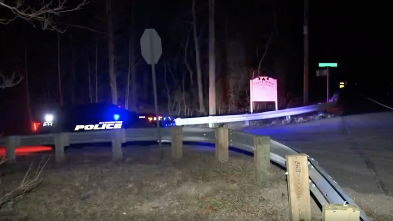 A police car is seen in the dark near a wooded area where a helicopter crashed.