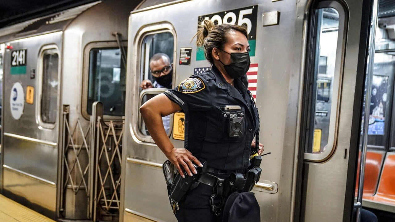A New York City Police Department officer and a subway conductor look down the subway platform.