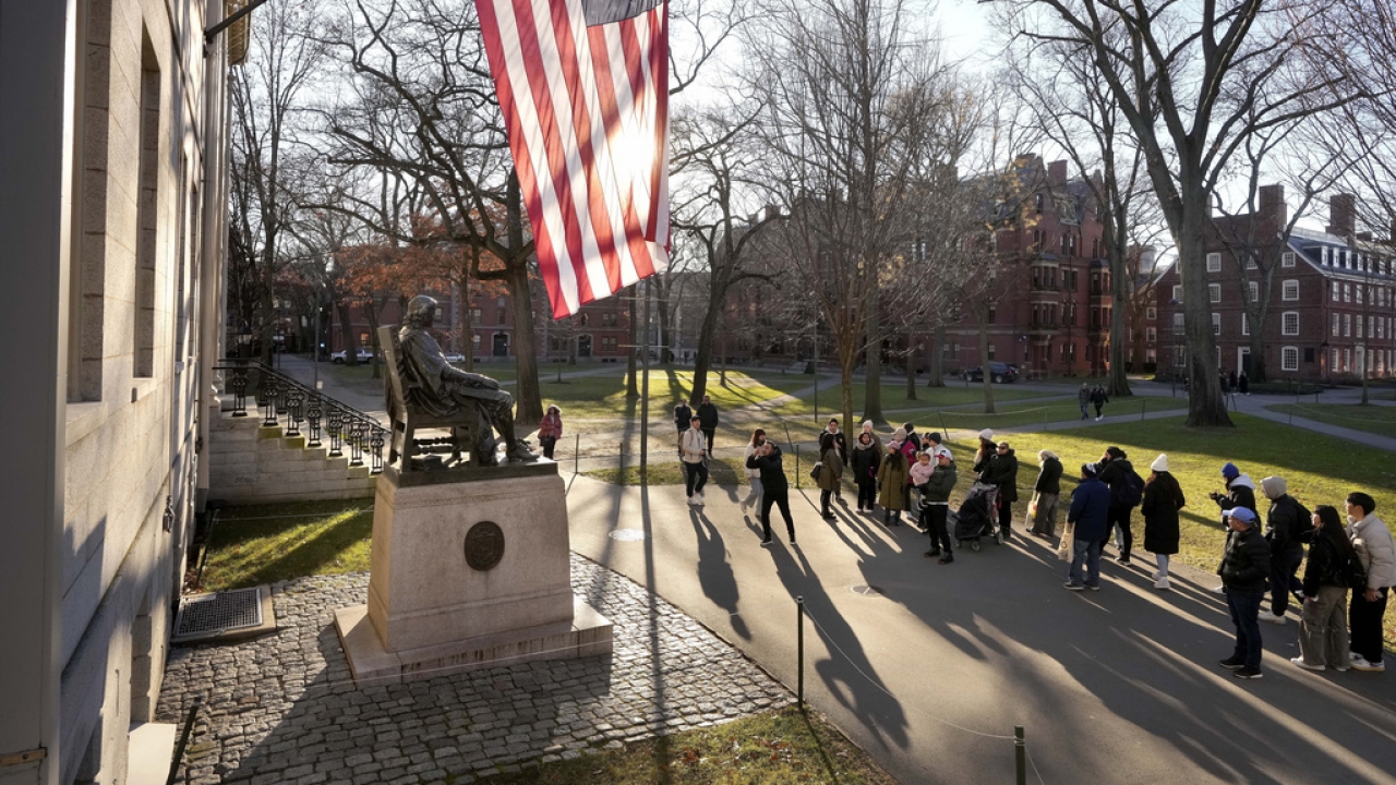 People take photos near a John Harvard statue on the Harvard University campus.