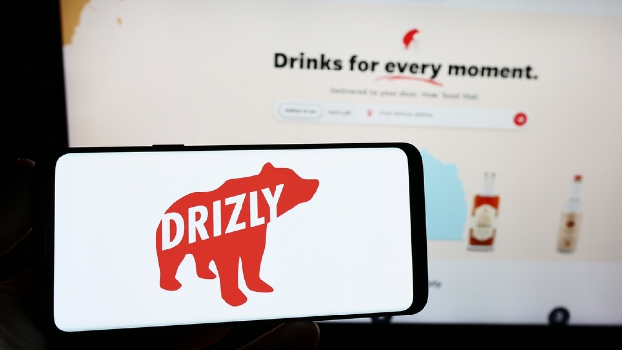 Person holding smartphone with logo of US alcohol delivery company Drizly on screen in front of website.