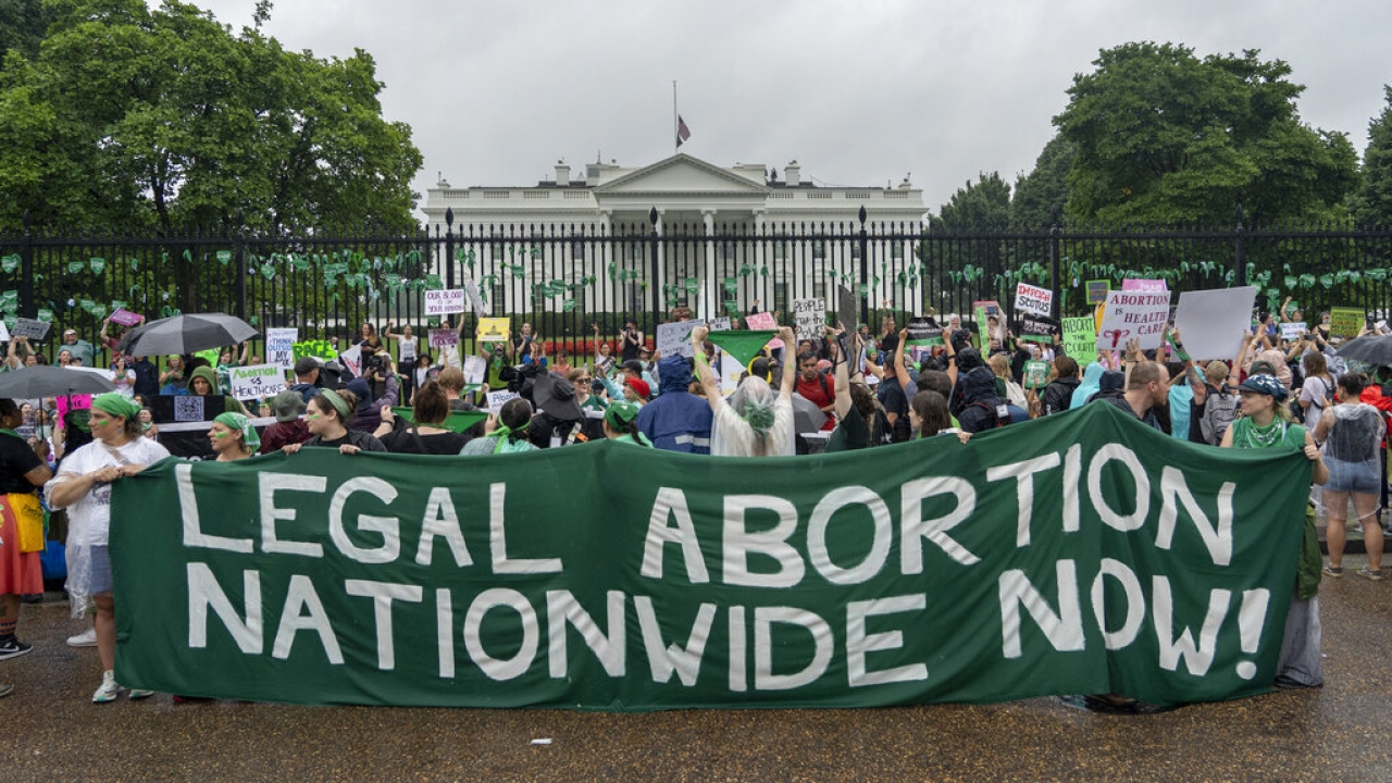 Abortion-rights protesters shout slogans and display banners after tying green flags to the fence of the White House.