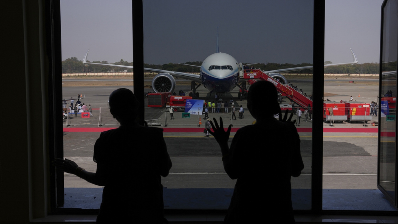 People look through glass at a Boeing plane on the tarmac