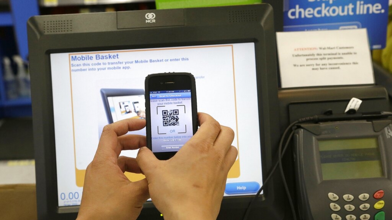 A Walmart representative demonstrates a Scan & Go mobile payment application on a smartphone.