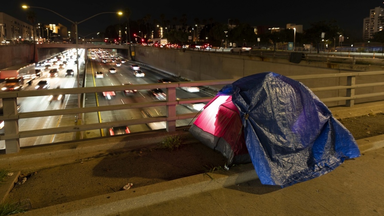 A tarp covers a portion of a homeless person's tent on a bridge overlooking the 101 Freeway in Los Angeles