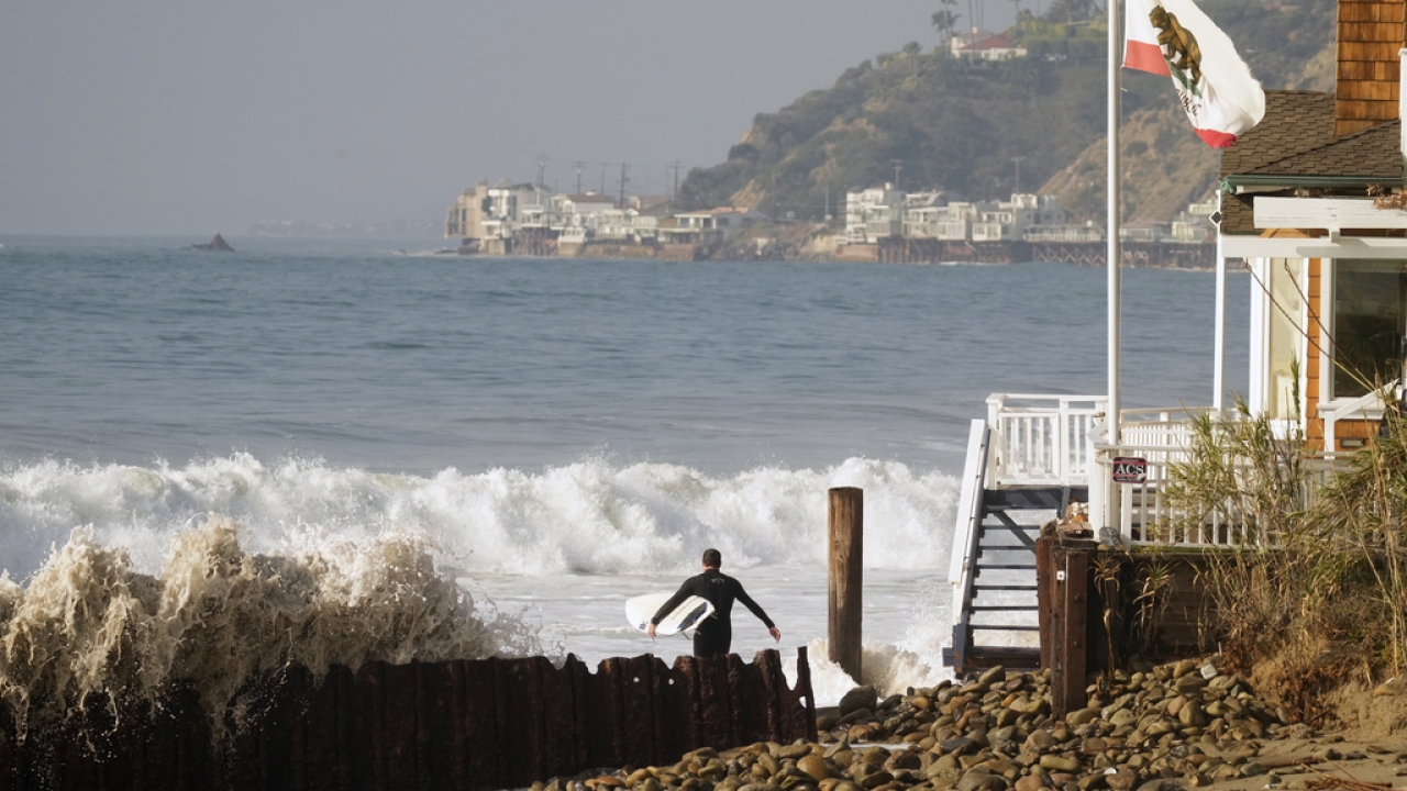 A surfer walks into the waves in Topanga Beach in Los Angeles.